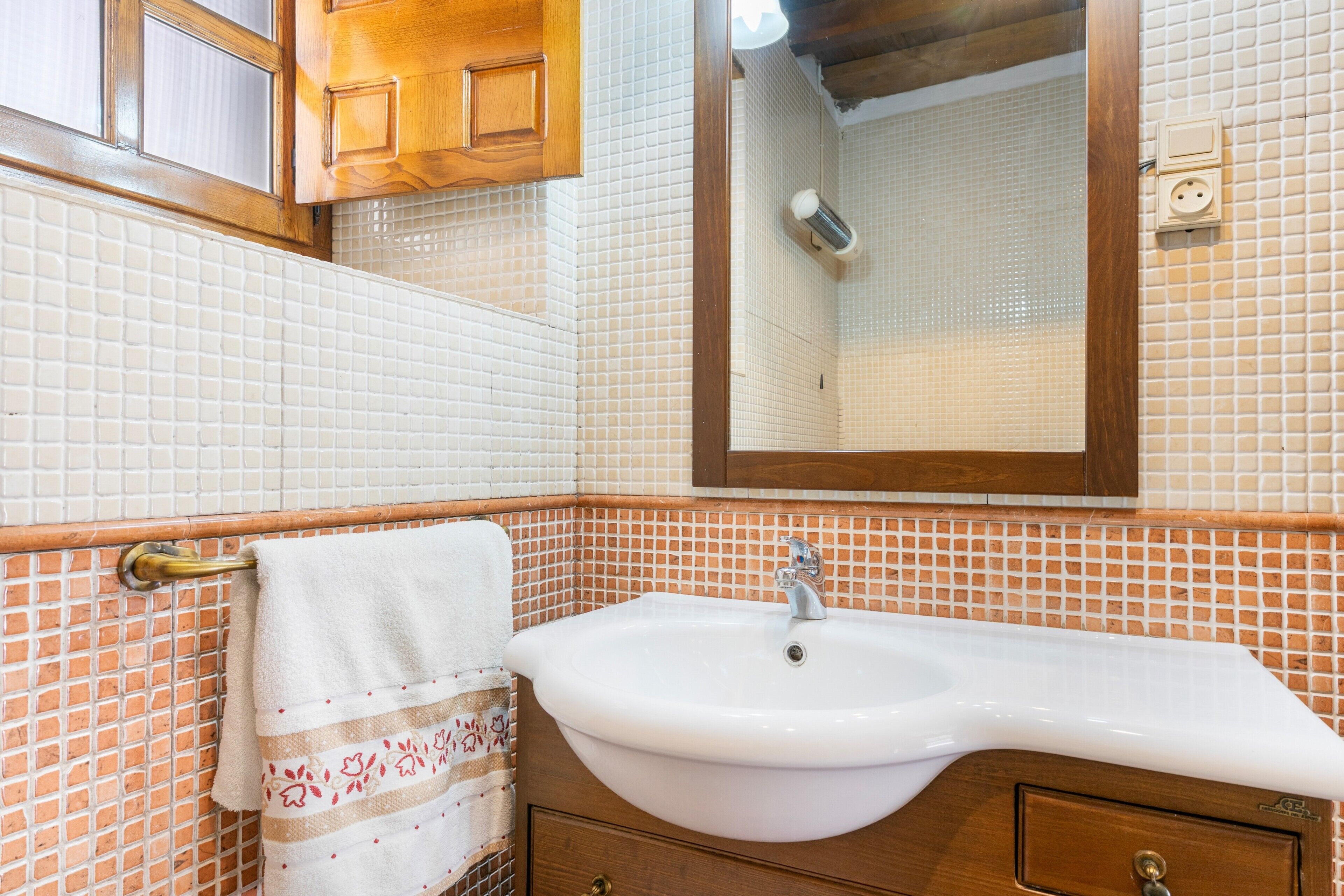 Un baño con lavamanos blanco, mueble de madera y espejo.