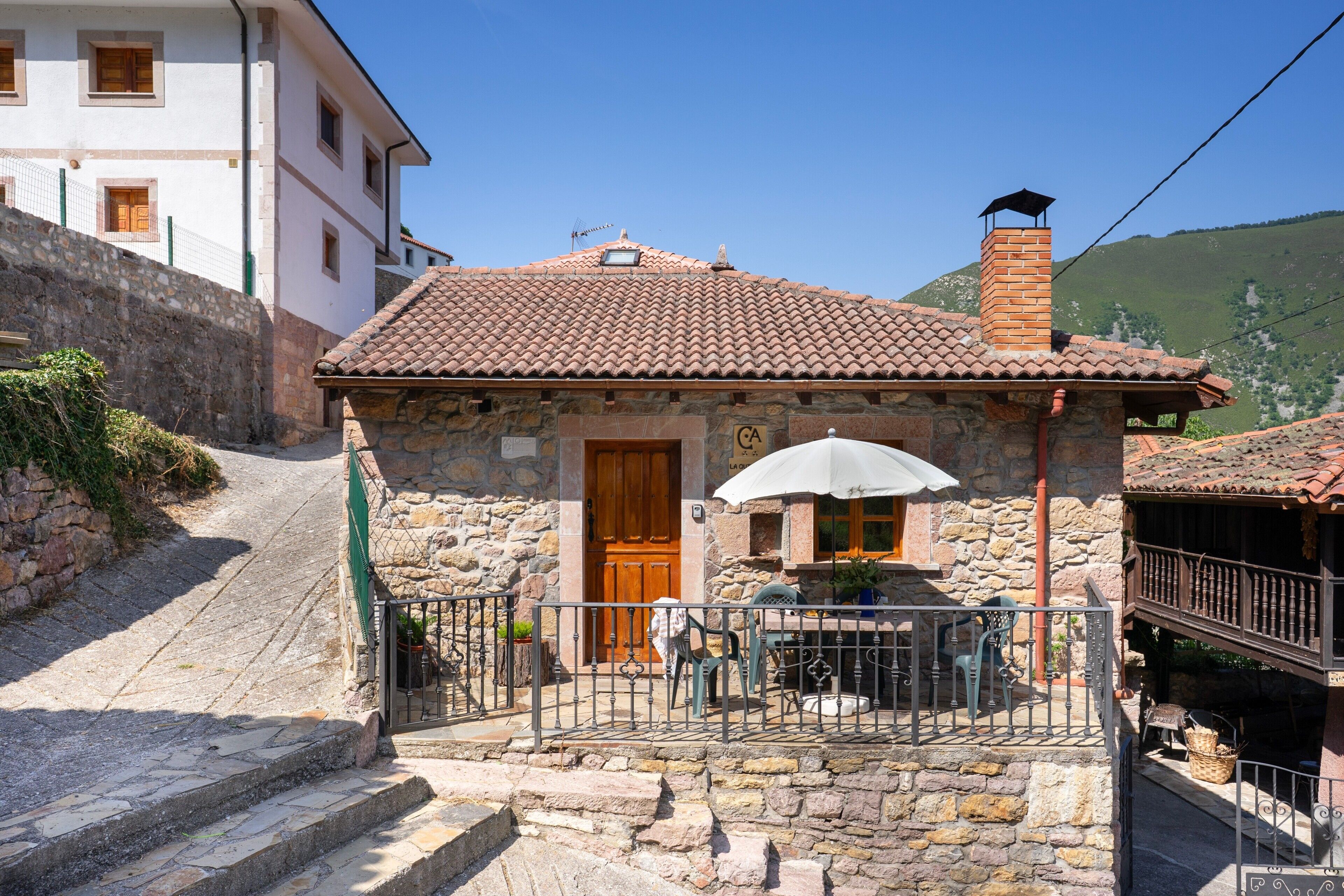 A stone building with a tiled roof, a wooden door, and a small patio with a table and chairs.