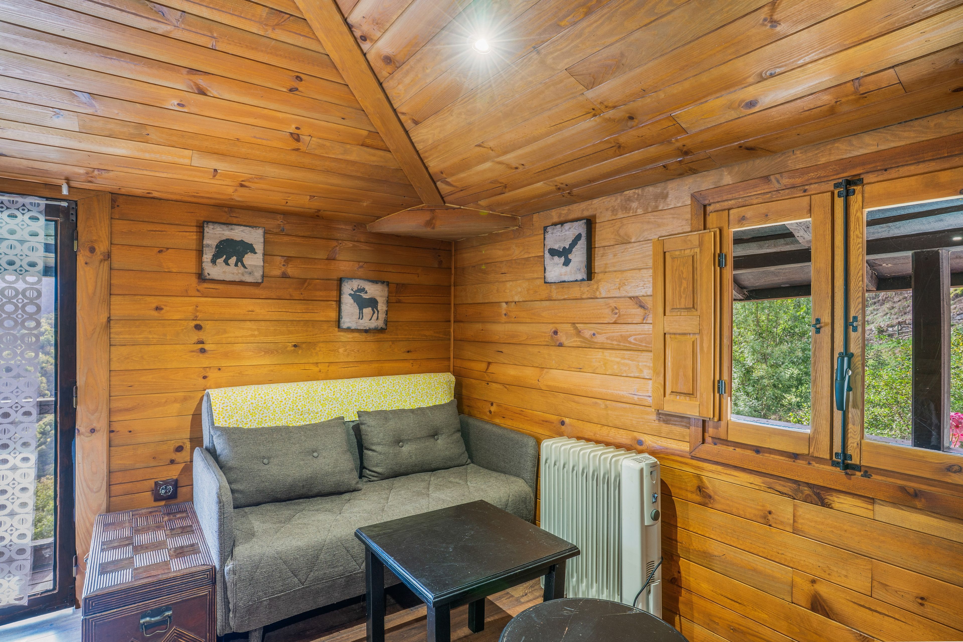 Interior acogedor de una cabaña con sofá, mesa y ventana con vistas a la vegetación.