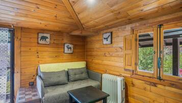 Interior acogedor de una cabaña con sofá, mesa y ventana con vistas a la vegetación.