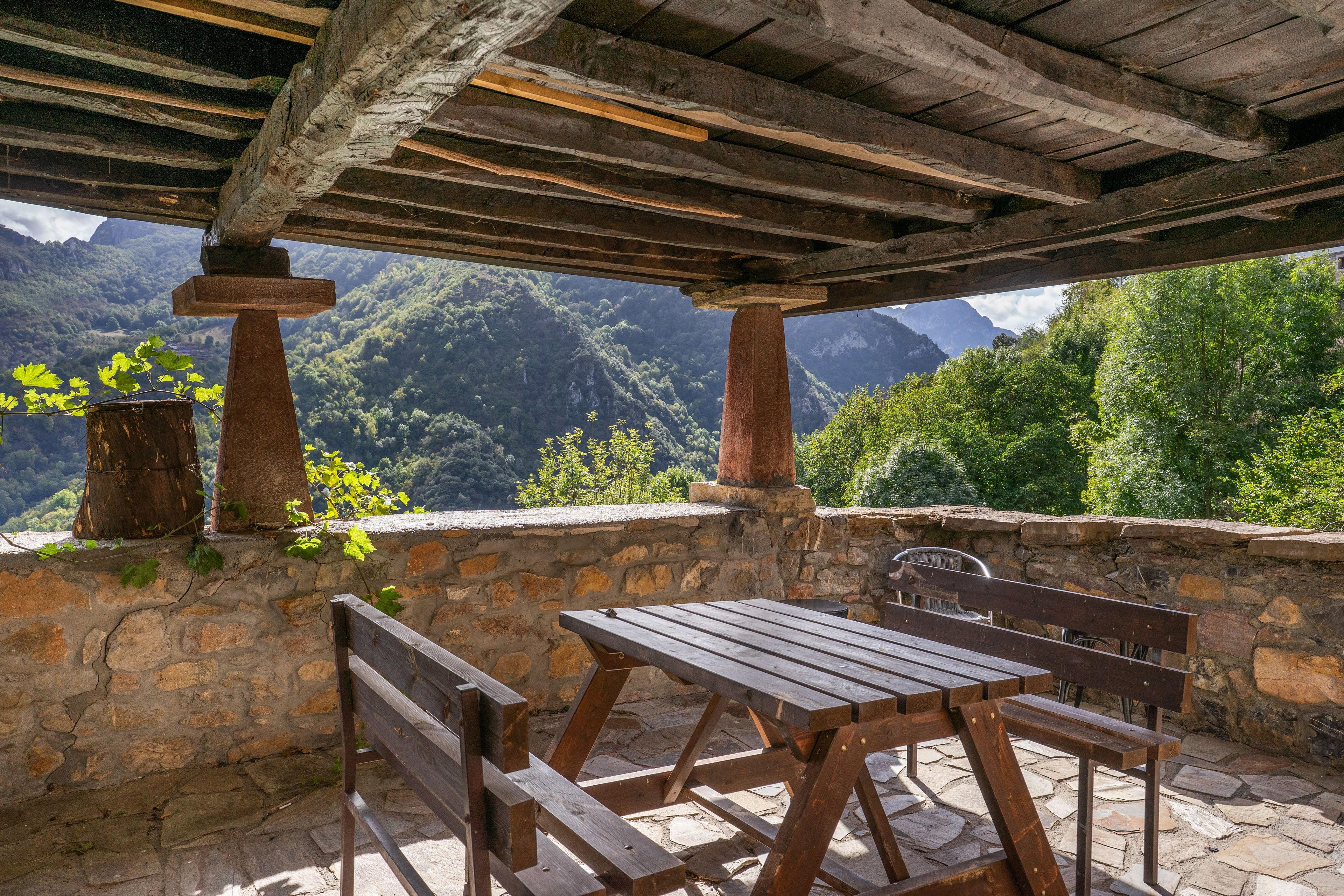 A wooden pergola with a stone wall and a table and bench set.