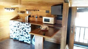 Un intérieur en bois avec un coin cuisine comprenant un four à micro-ondes, un évier et une nappe à motifs.