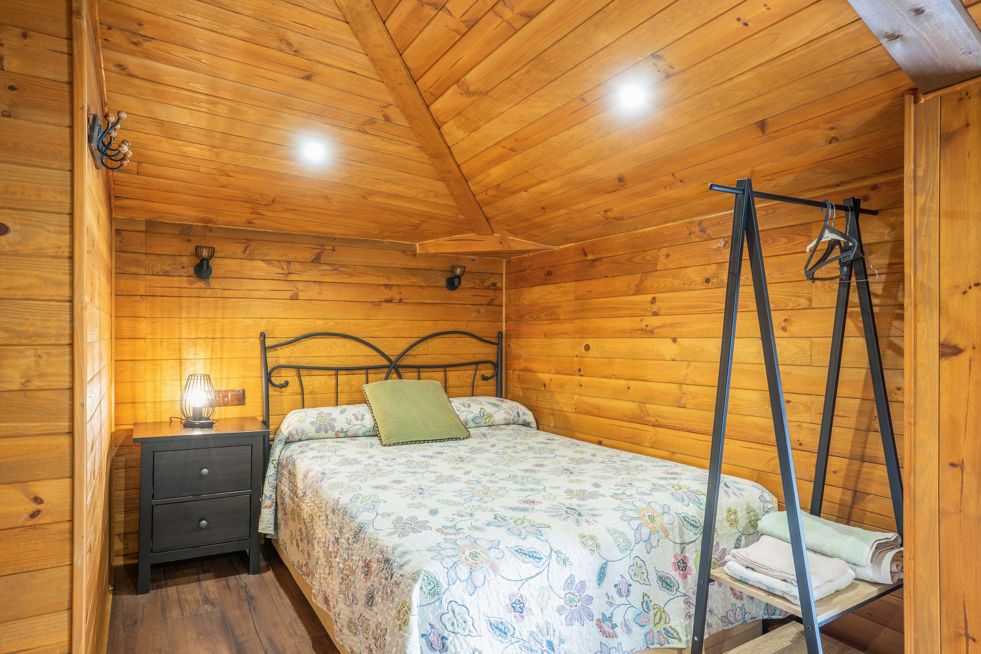 Una habitación con paneles de madera, una cama, una mesita de noche, una lámpara colgante y un ventilador de techo.