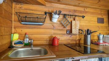A wooden cabin kitchen with a sink, a red kettle, a coffee pot, and various utensils hanging on the wall.