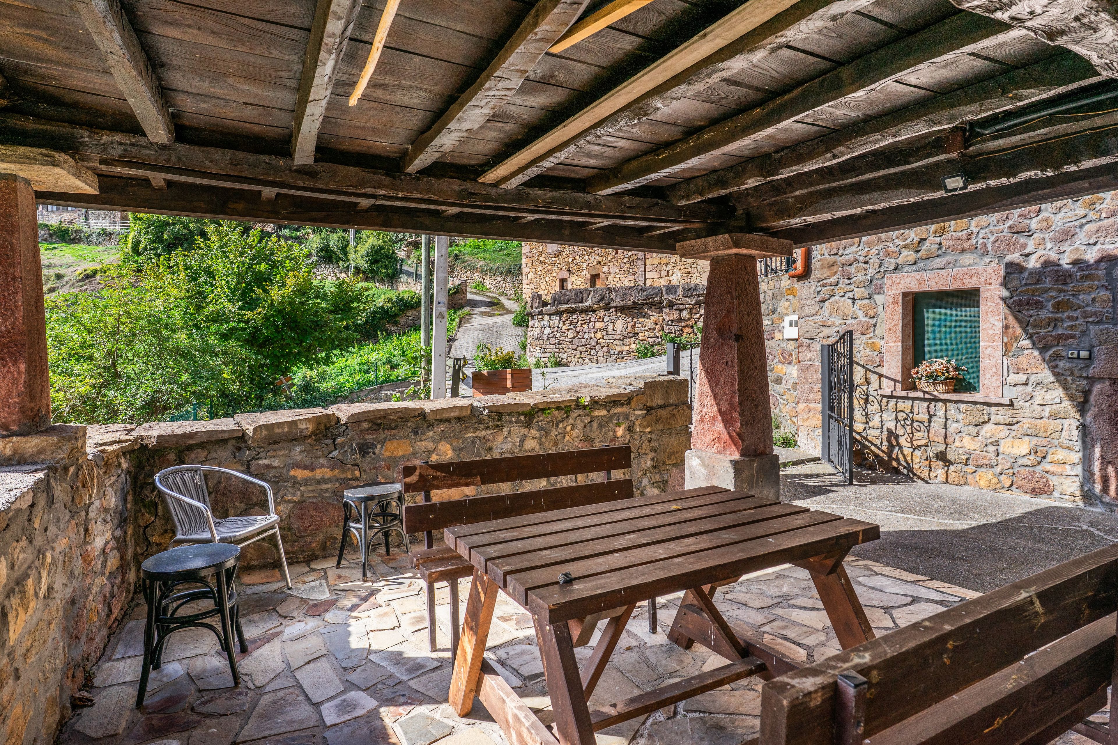Un patio exterior con suelo de piedra, bancos de madera y una mesa.