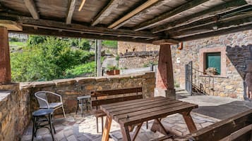 Un patio exterior con suelo de piedra, bancos de madera y una mesa.
