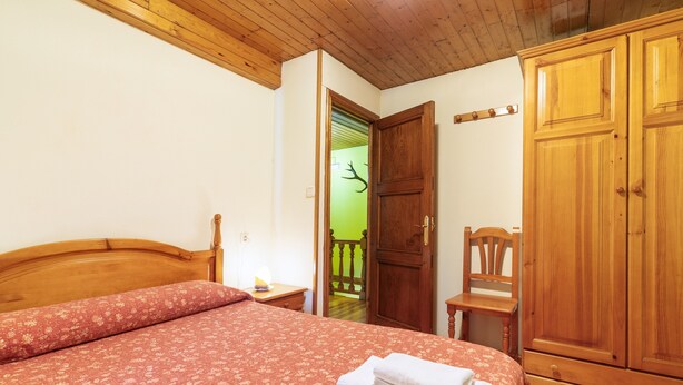 A bedroom with a wooden bed, a wooden wardrobe, and a green door leading to a balcony. - Casa de Aldea La Besana (Las Viñas)