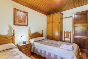 Un dormitorio con dos camas de madera, una mesita de noche, un armario de madera y una silla.