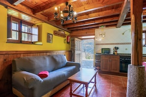 A cozy room with a wooden ceiling, a sofa, a small table, and a kitchen area with cabinets and appliances.