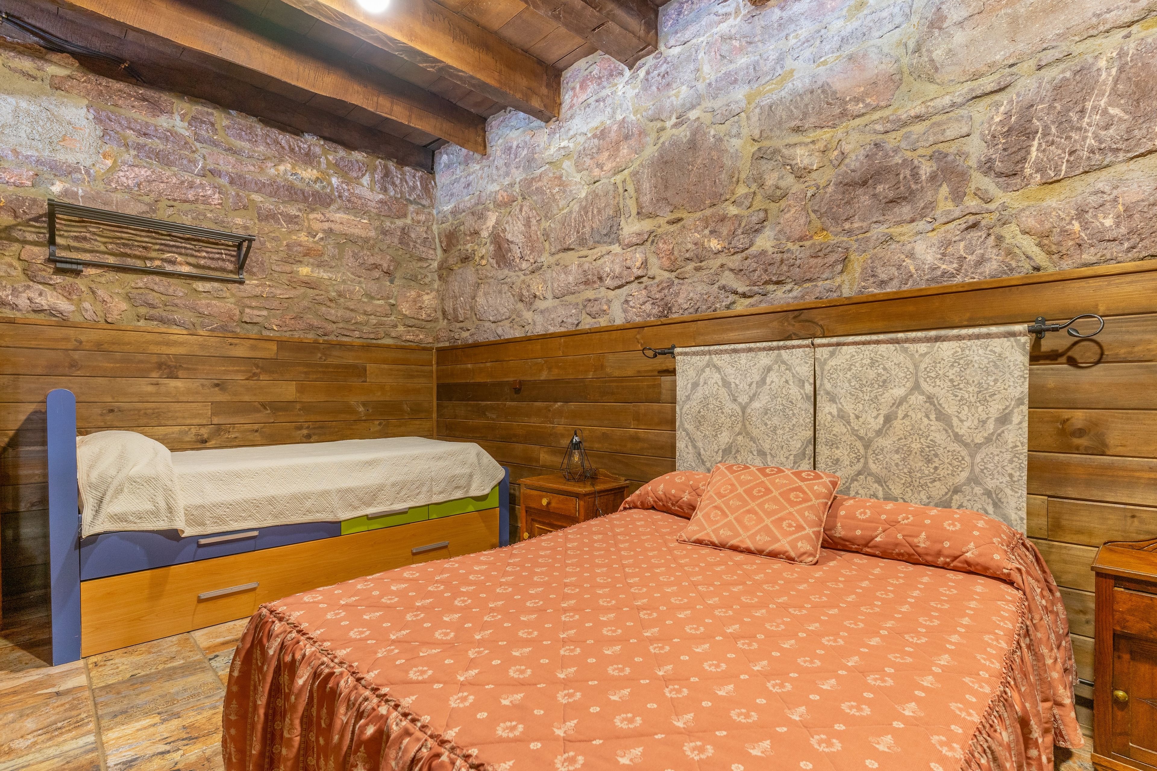 Une chambre à coucher rustique avec un lit en bois, une table de chevet et un mur en pierre.