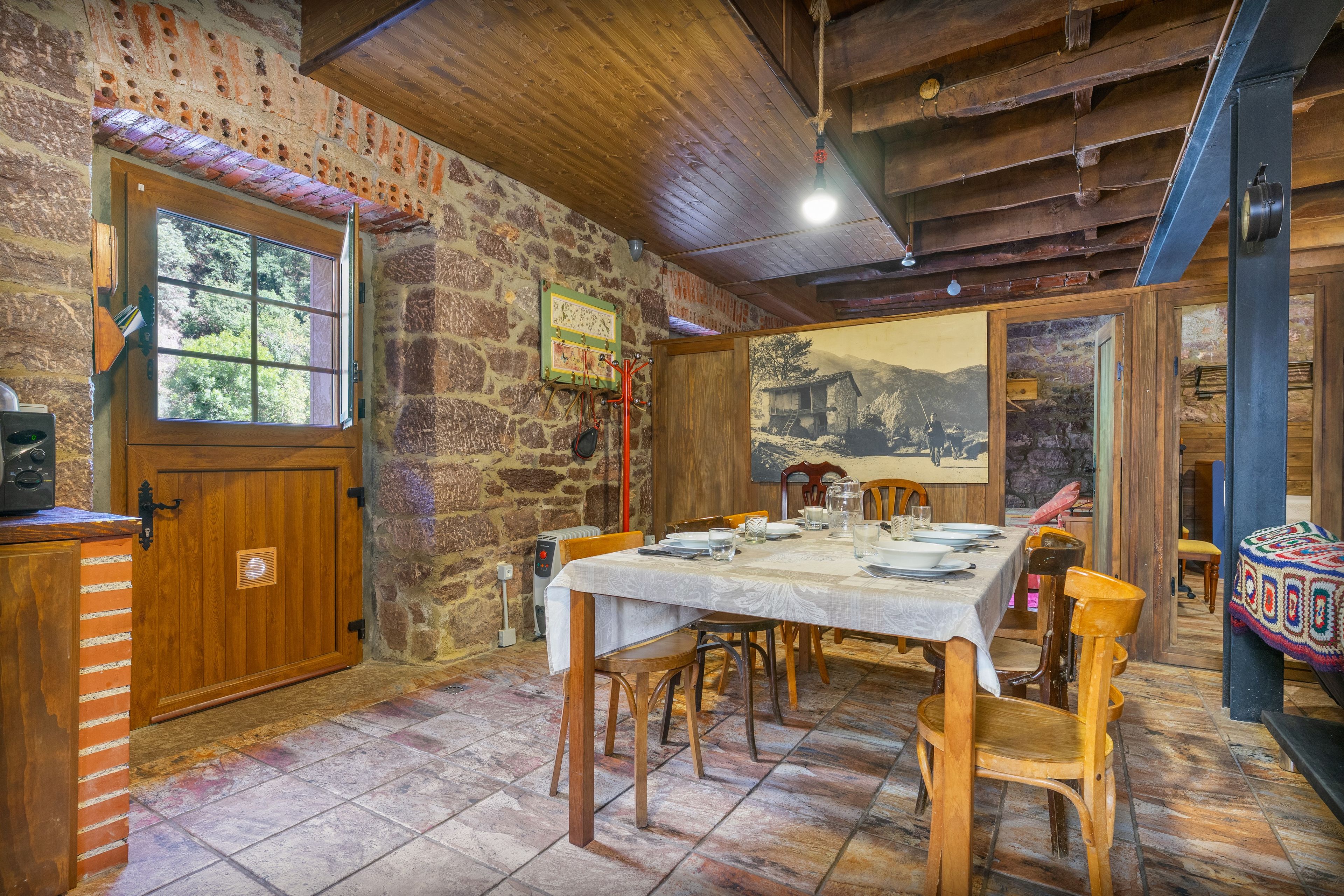 Un coin repas rustique avec un mur en pierre, un plafond en bois et une table dressée pour quatre personnes.