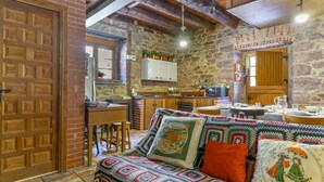 Un interior acogedor con una puerta de madera, un sofá estampado, una pared de piedra y una zona de cocina con armarios de madera y una lámpara colgante.