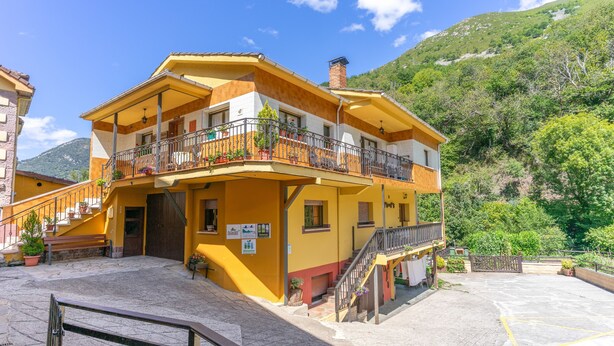 Un edificio de dos pisos con fachada amarilla, un balcón con barandilla metálica y una escalera que lleva a la entrada.