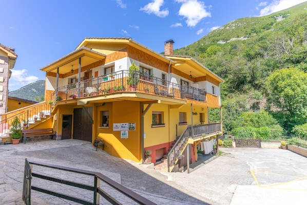 A two-story building with a yellow facade, a balcony with a metal railing, and a staircase leading to the entrance.