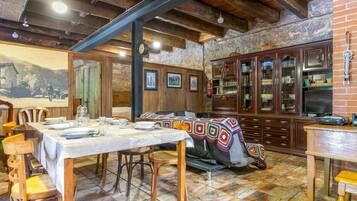 A dining area with a table set for two, wooden chairs, a patterned tablecloth, and a cabinet with glass doors.