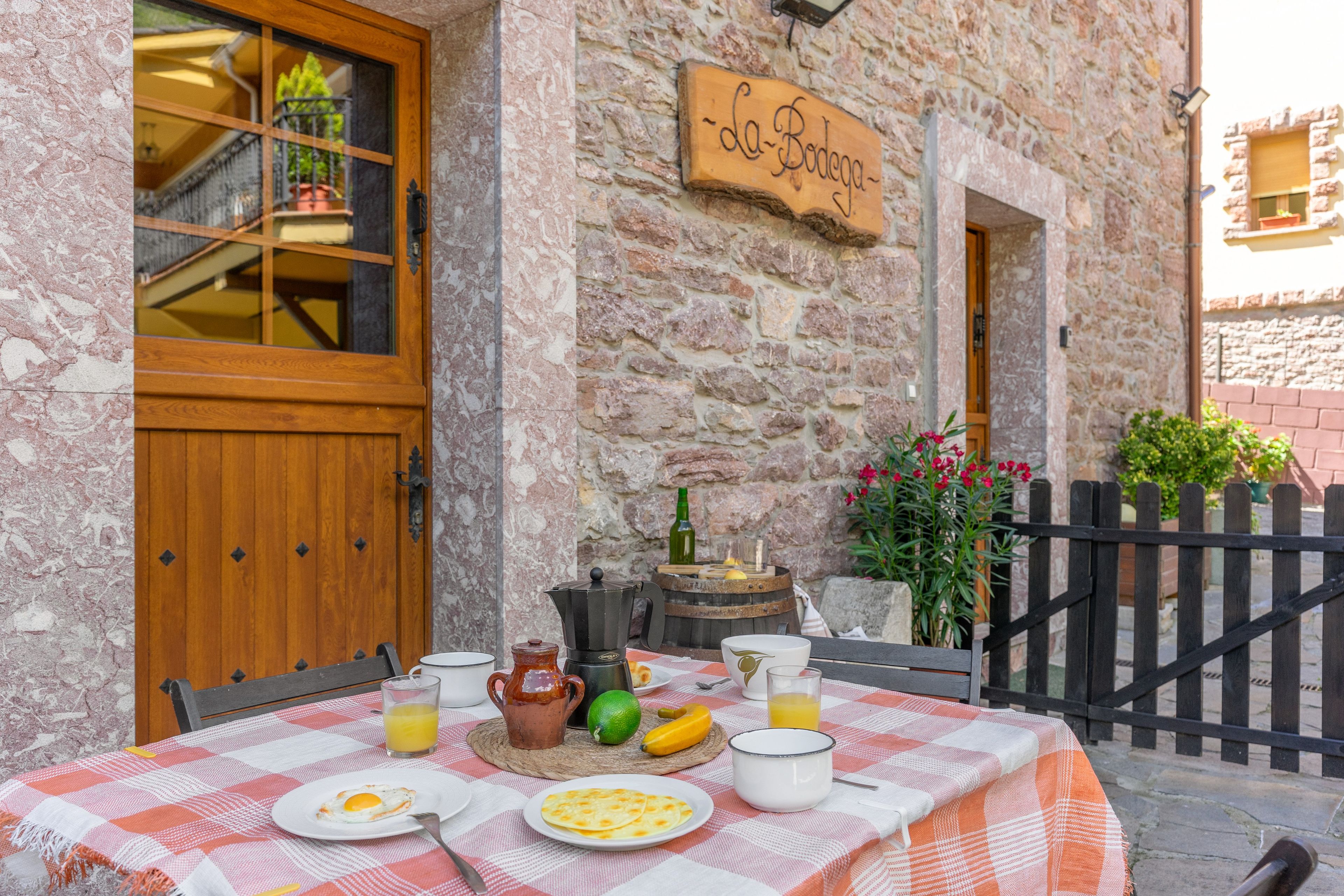 Una mesa de desayuno dispuesta al aire libre frente a un edificio de piedra con una puerta de madera y un letrero que dice 'La Bodega'.