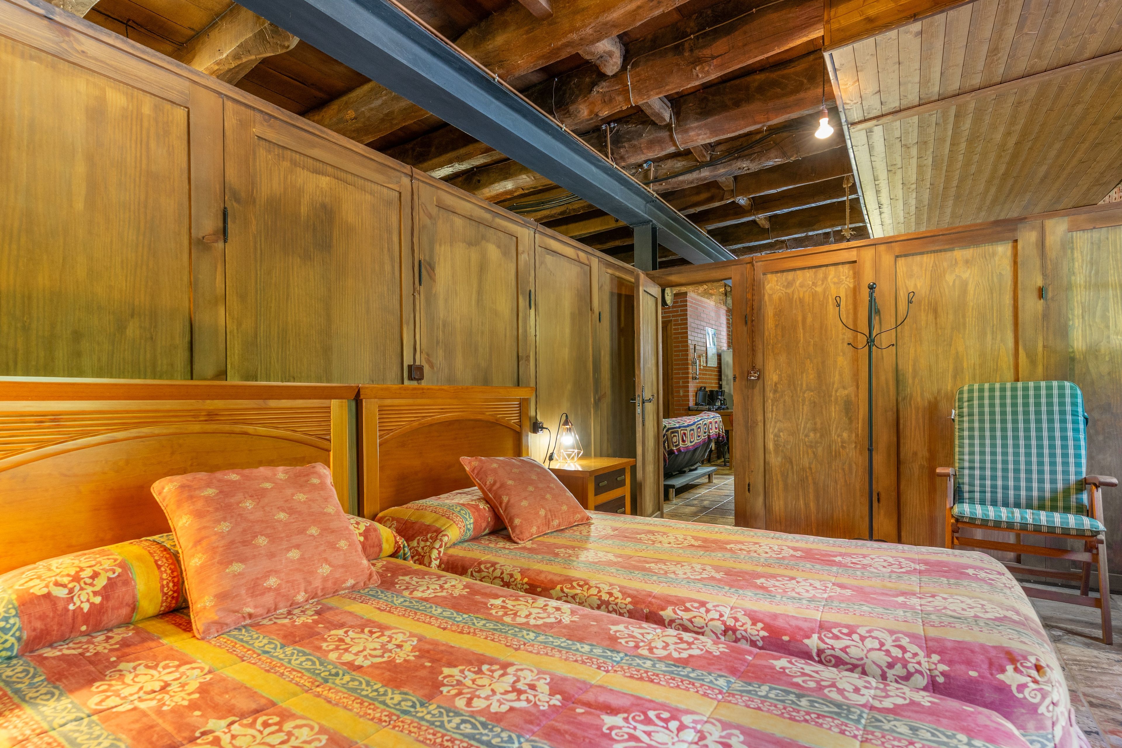 Een kamer met een houten bed, een stoel en een bakstenen muur.