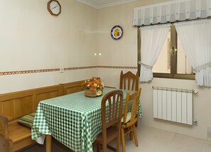 Un comedor con una mesa dispuesta para dos personas, un reloj en la pared y un radiador debajo de una ventana con cortinas.