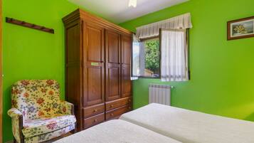 A room with a bed, a wooden wardrobe, a floral armchair, and a window with curtains.