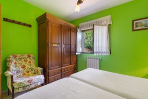 A room with a bed, a wooden wardrobe, a floral armchair, and a window with curtains. - Apartment 'La Veiga 1' (La Riera)