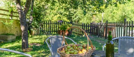 A picnic table with a basket of fruit, a bottle, and metal chairs.