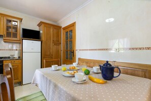 A kitchen with wooden cabinets, a refrigerator, a dining table with breakfast items, and a television on a stand. - Apartment 'La Veiga 1' (La Riera)