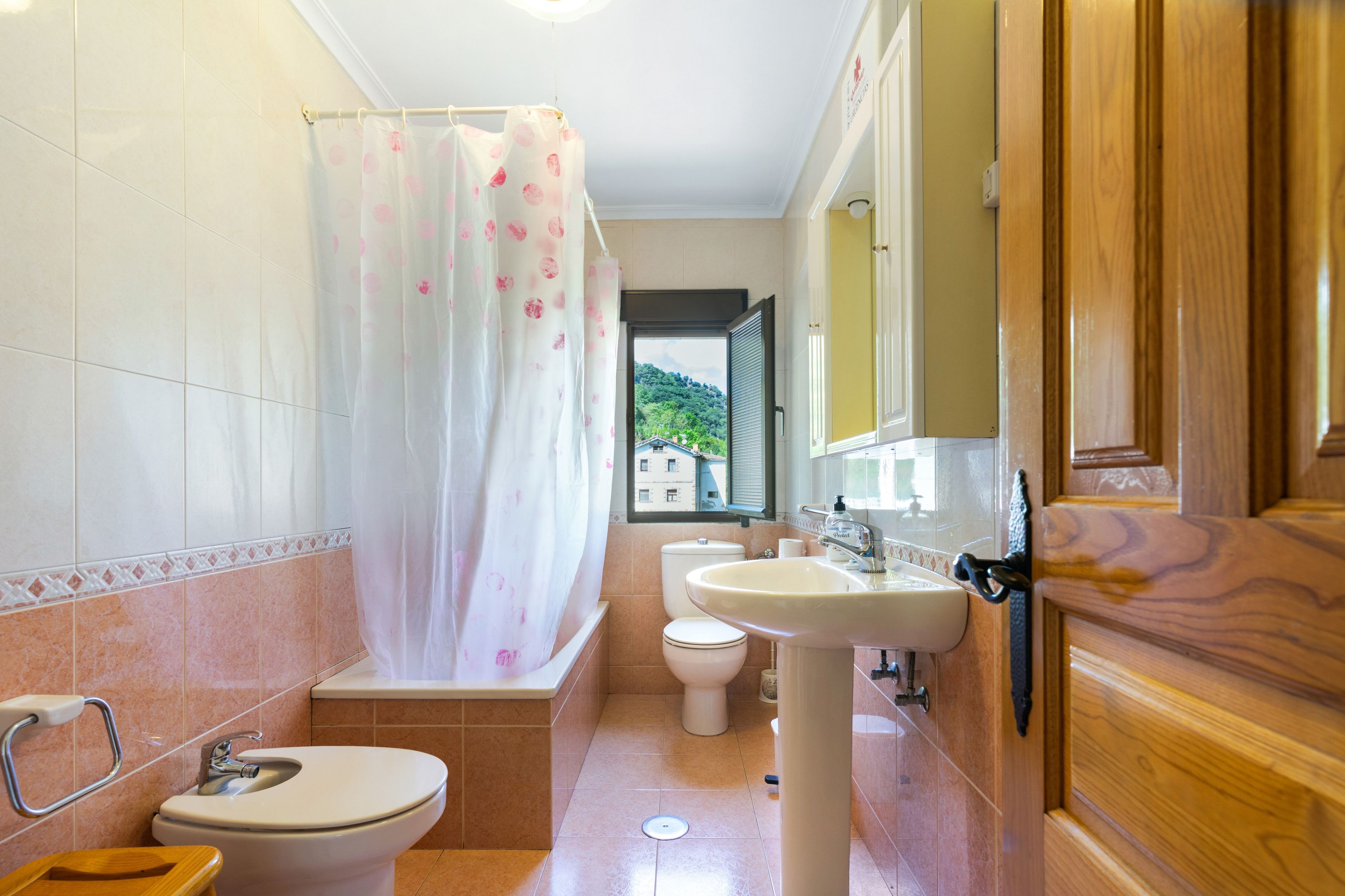 A bathroom with a shower curtain, toilet, sink, and wooden door.