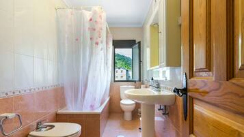 A bathroom with a shower curtain, toilet, sink, and wooden door.