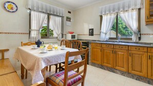 Une cuisine avec des meubles de rangement en bois, une table à manger avec des chaises et une fenêtre avec des rideaux.