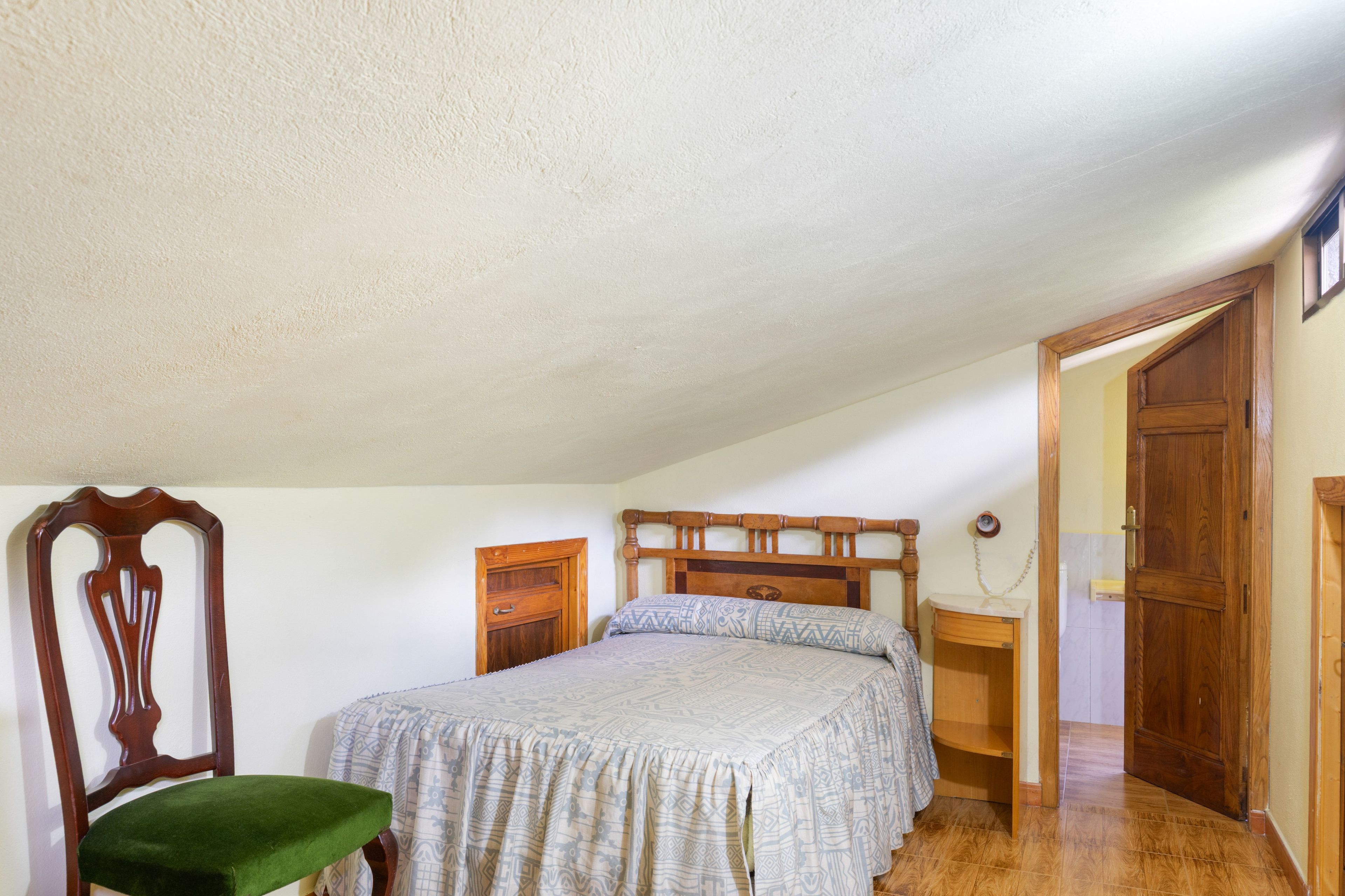 A bedroom with a bed, a wooden chair, a bedside table, and a wardrobe.