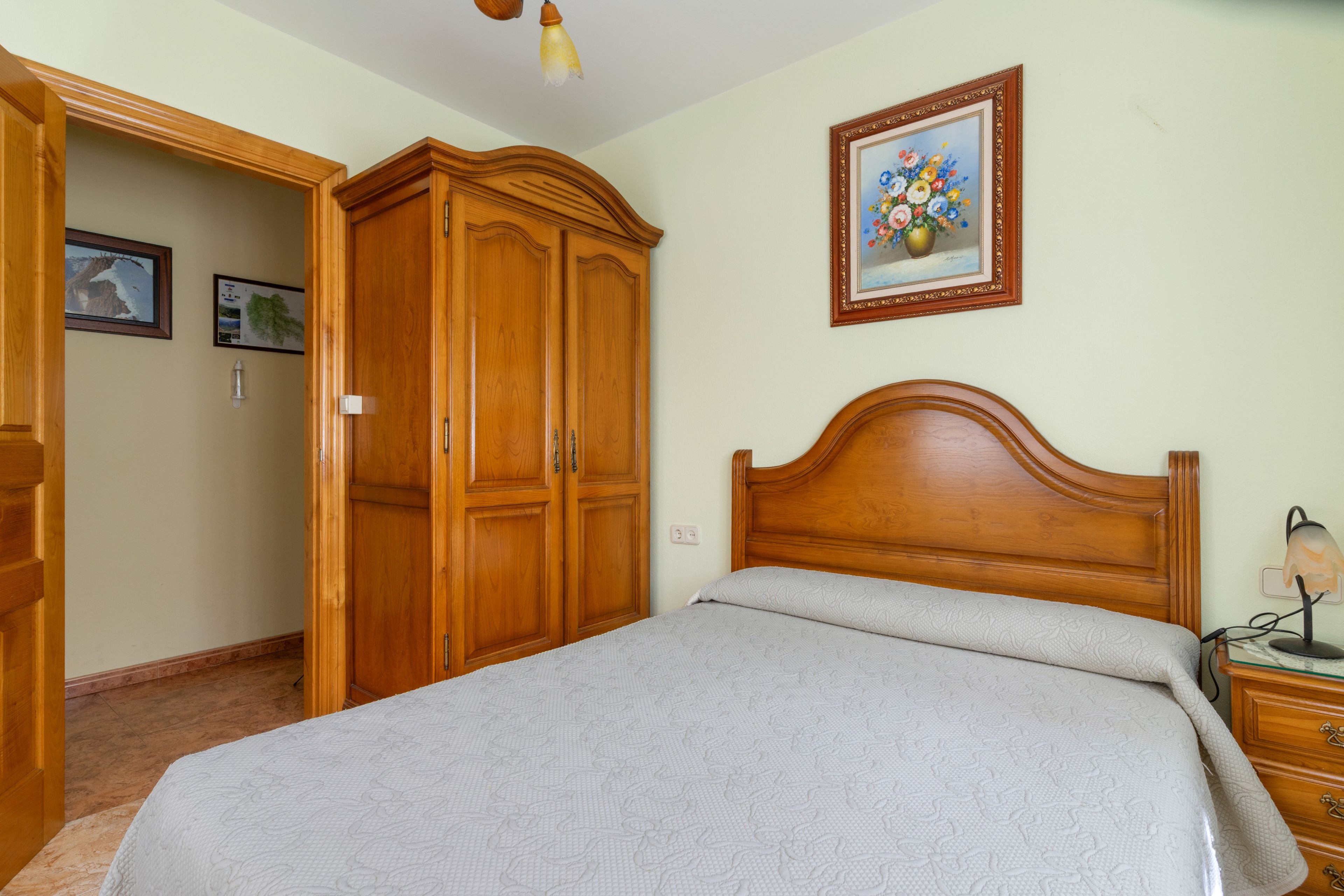 Una camera da letto con un letto in legno, un armadio, un comodino e una lampada a muro.
