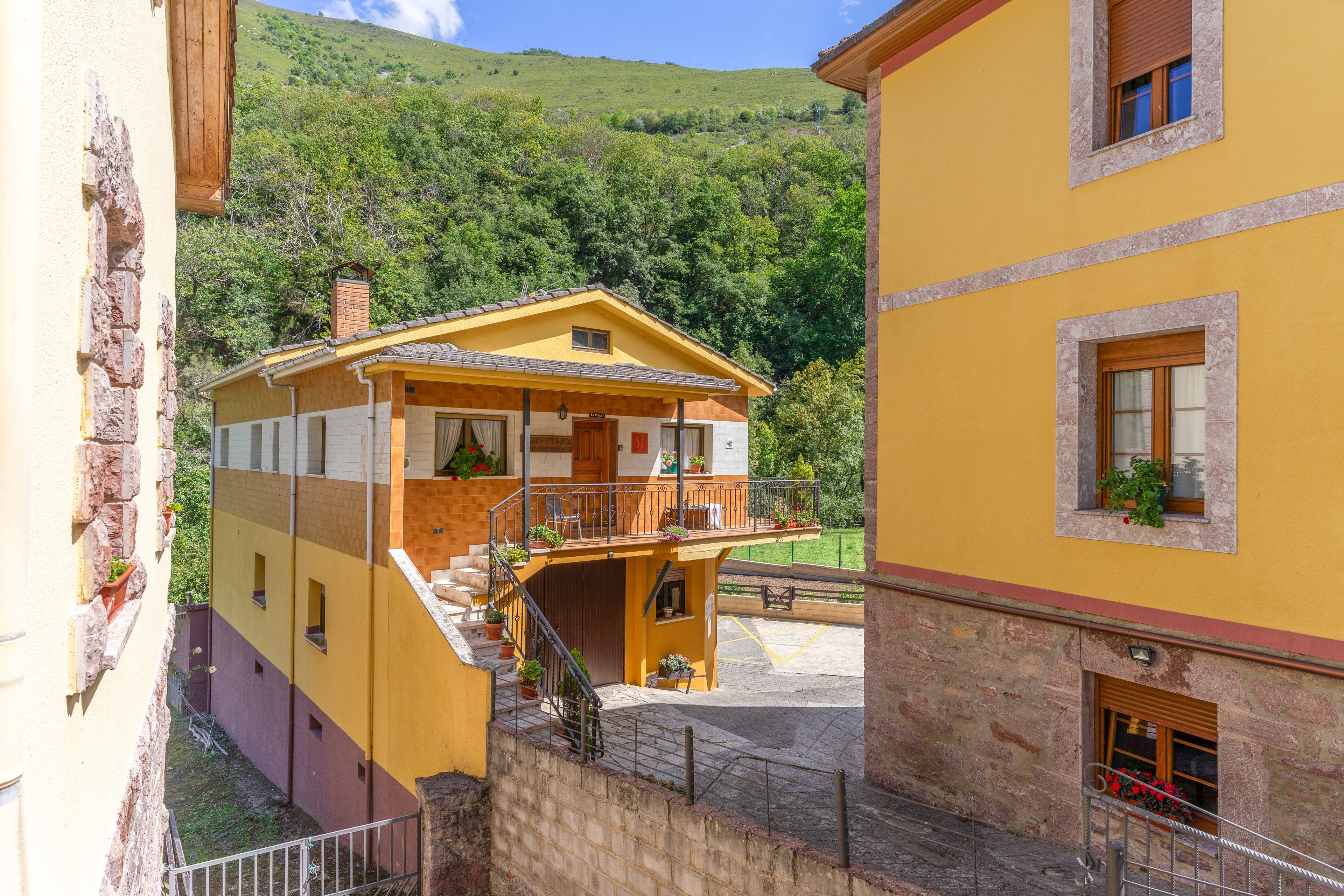 Un bâtiment jaune doté d’un balcon, d’un escalier et offrant une vue sur une colline verdoyante.
