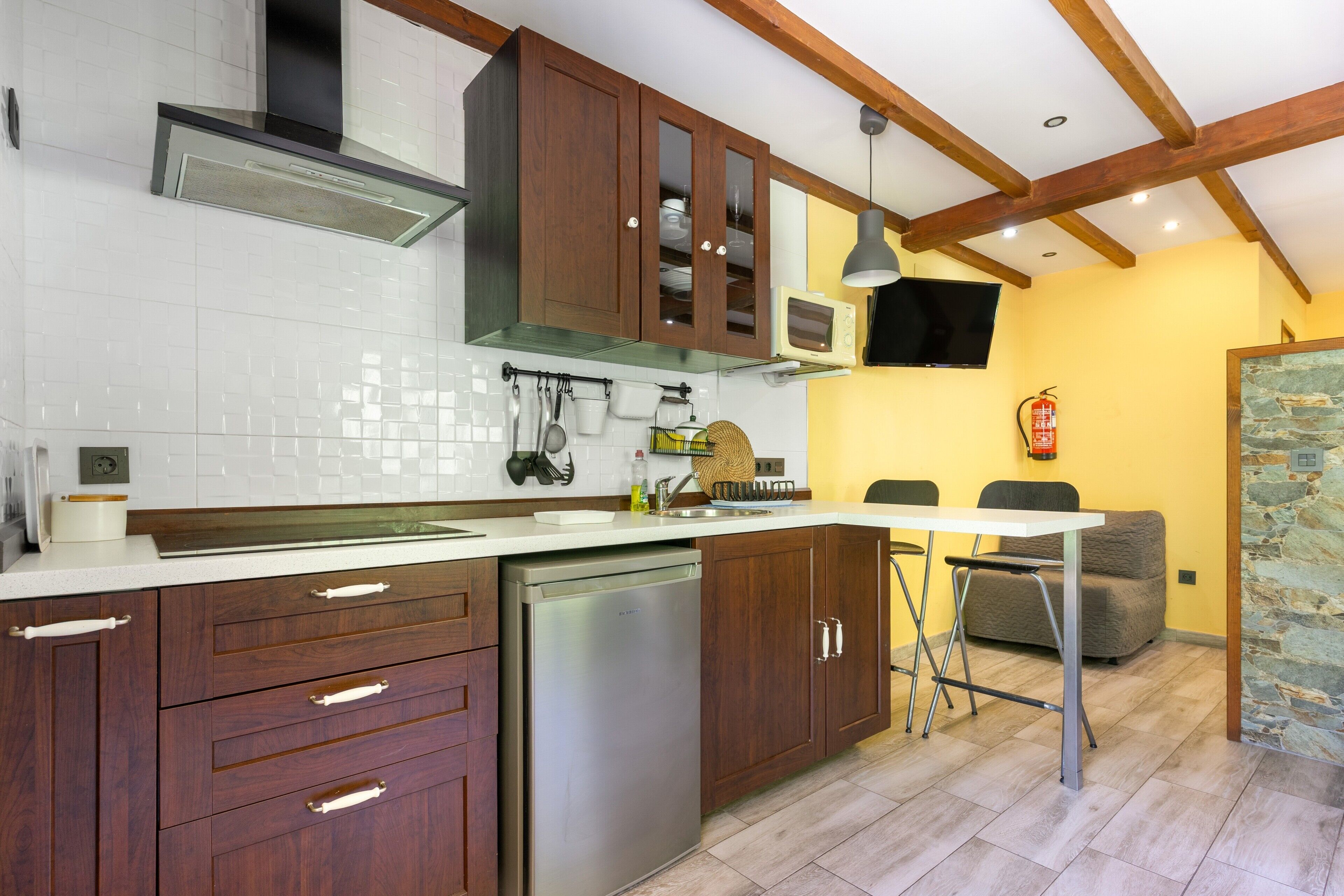 Una cocina con armarios de madera, lavavajillas, microondas y un comedor con mesa y sillas.