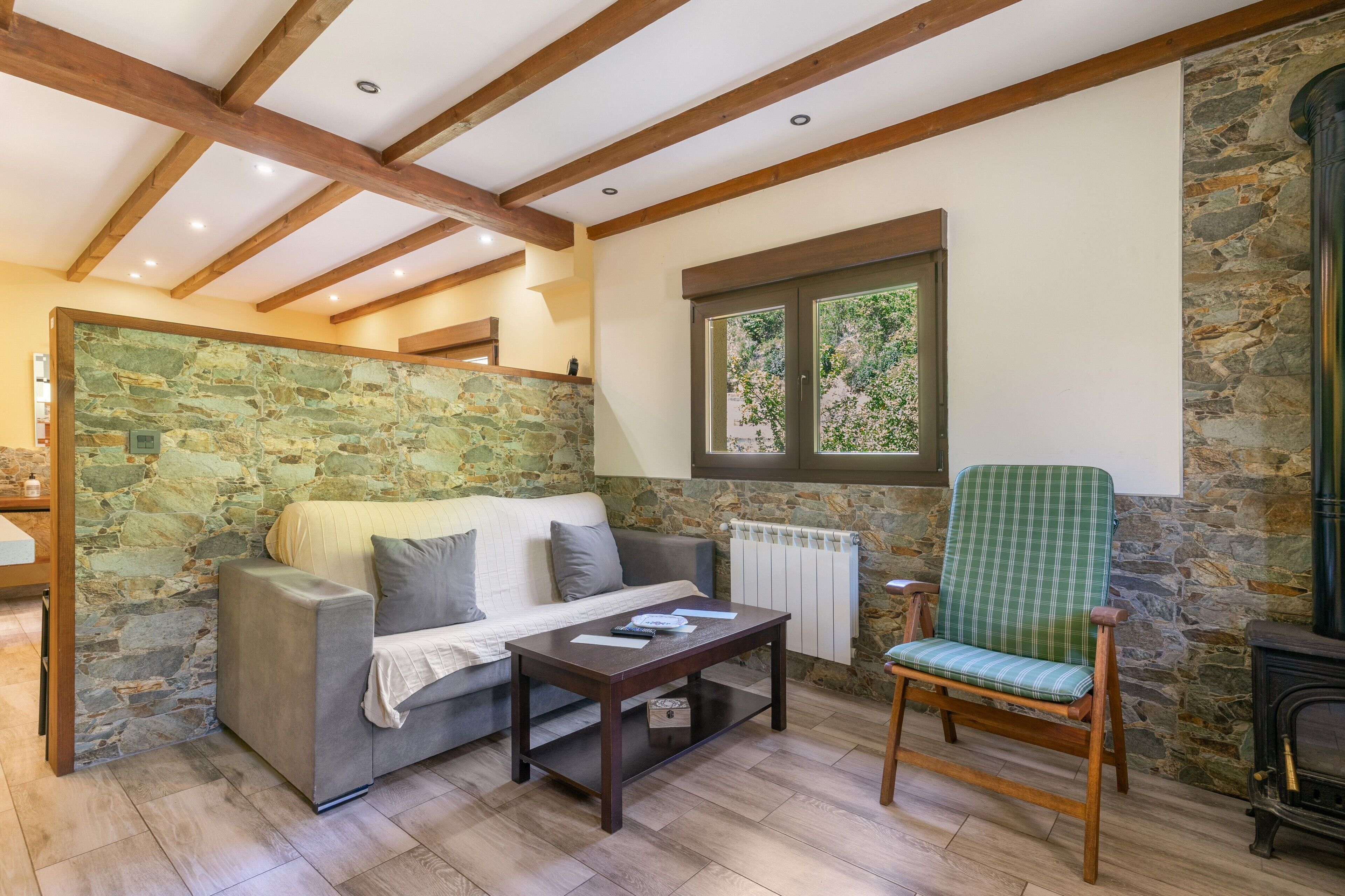 Una sala de estar acogedora con pared de piedra, vigas de madera, un sofá, un sillón y una chimenea.
