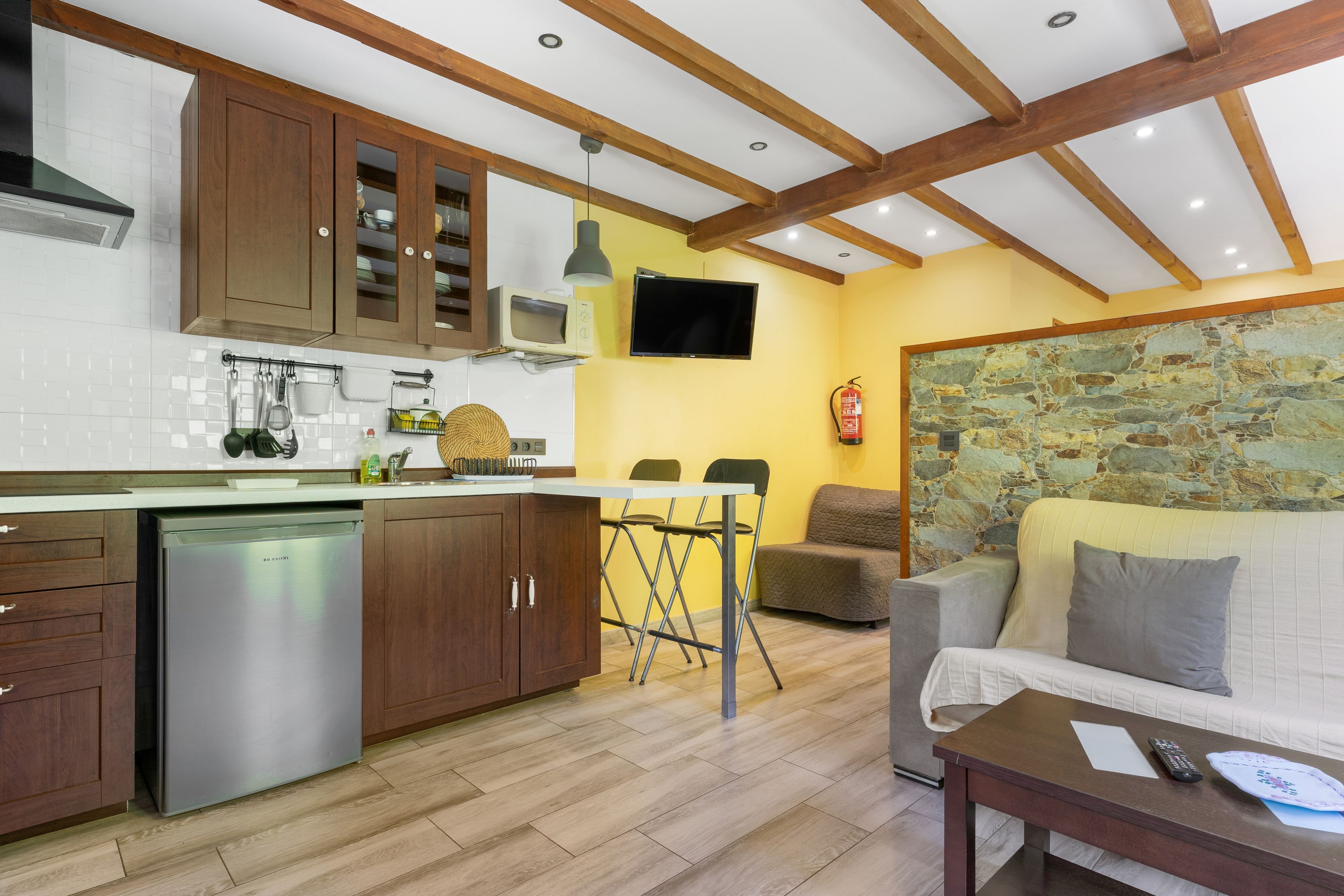 Una cocina con armarios de madera, un microondas integrado y una zona de comedor con pared de piedra.