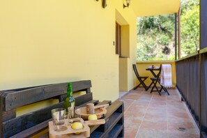 A wooden bench with a bottle and glasses on it, and a table with a cloth in the background.