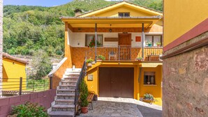Un bâtiment jaune avec un escalier menant à un balcon, entouré de verdure et de collines.