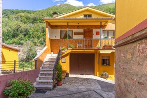 Edificio amarillo con una escalera que conduce a un balcón, rodeado de vegetación y colinas.