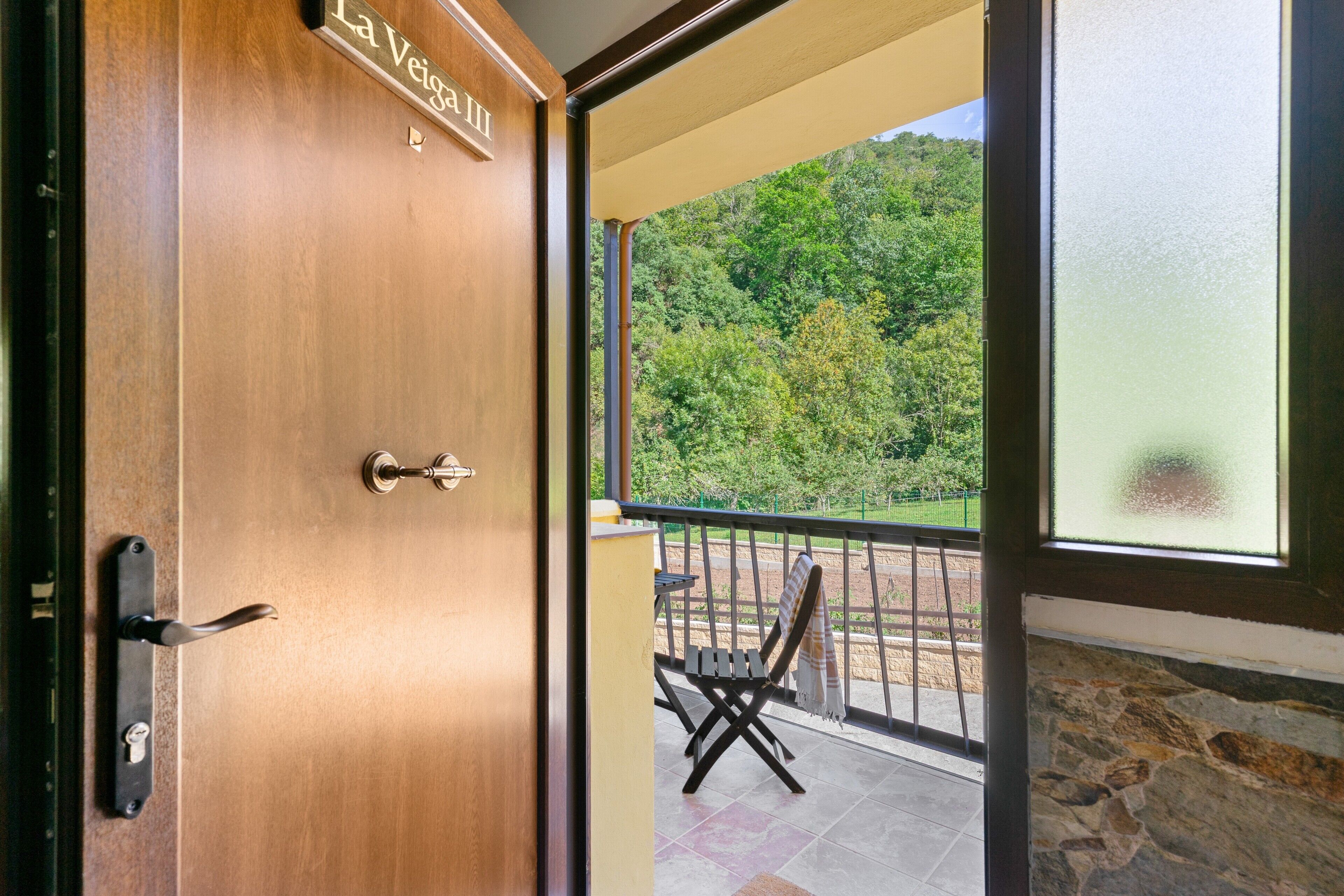 Una puerta de madera con un letrero que dice 'La Veiga III' y una vista de un balcón con una silla y una mesa.