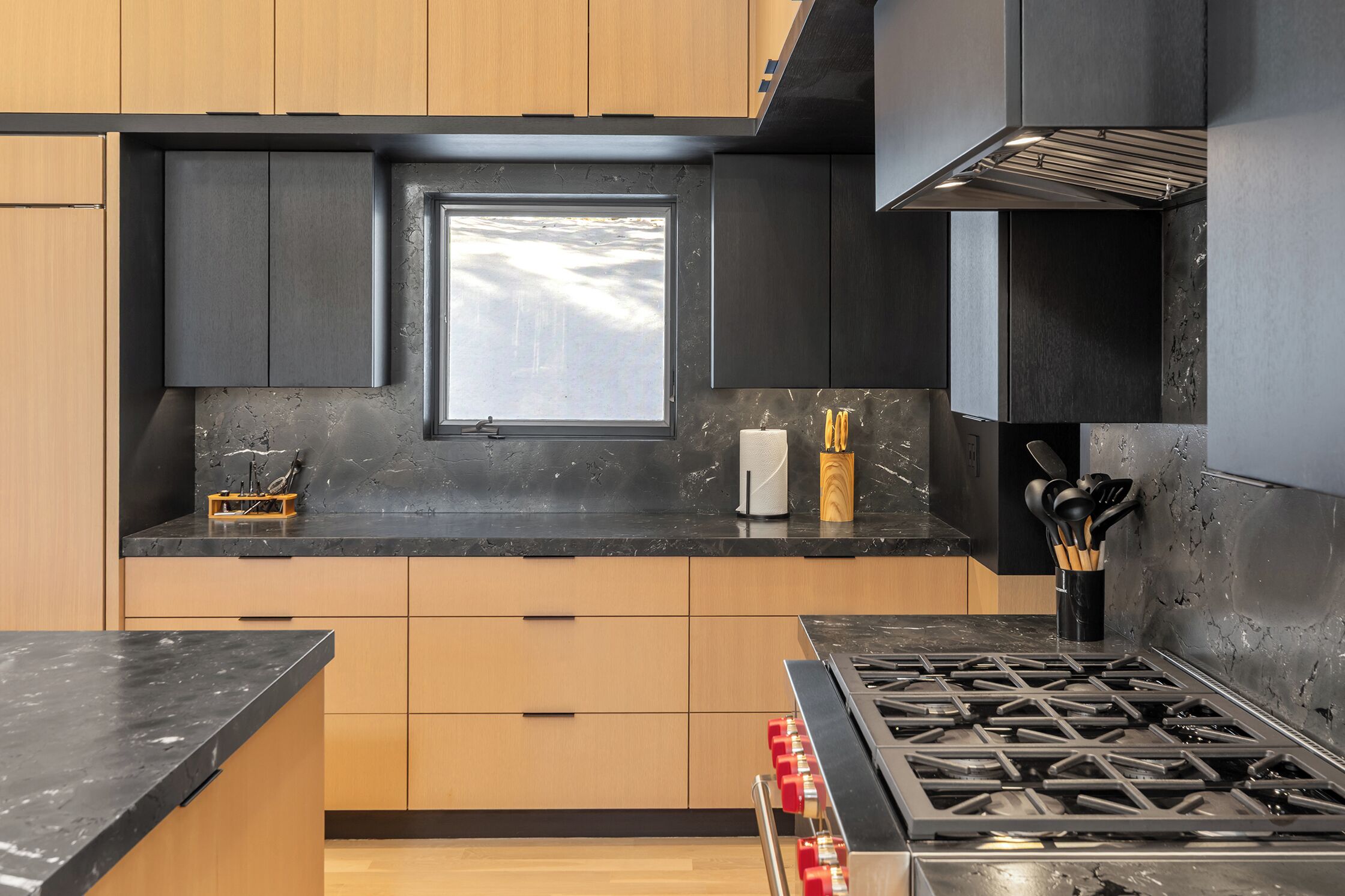 A modern kitchen with a gas stove, wooden cabinets, a window, and a marble countertop.