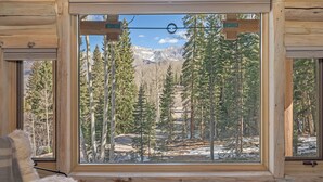Eine Blockhütte mit einem großen Fenster, das einen Blick auf den Wald und die Berge freigibt.