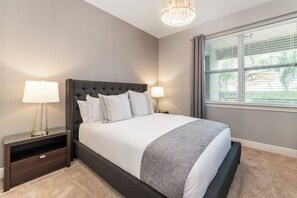 Ein ordentlich eingerichtetes Schlafzimmer mit einem großen Bett, zwei Nachttischen und einem Fenster mit Jalousien.