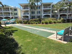 A courtyard with a shuffleboard court, outdoor seating, and a multi-story building with balconies.
