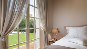 Een hotelkamer met een groot raam, een bed, een nachtkastje met lamp en uitzicht op een tuin.