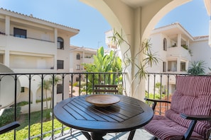 A balcony with a round table and a striped chair, surrounded by greenery and buildings. - Sun & Beach Apartment in Torremolinos, just 150m from the beach (Torremolinos)