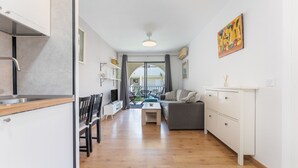 Une cuisine moderne avec des meubles blancs, un coin repas avec une table et des chaises, un canapé gris et, vue à travers une porte vitrée, un patio extérieur.