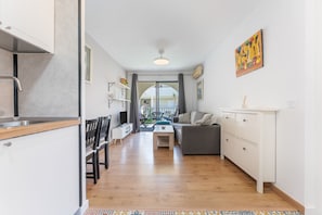 A modern kitchen with white cabinets, a dining area with a table and chairs, a gray sofa, and a view through a glass door to an outdoor patio. - Sun & Beach Apartment in Torremolinos, just 150m from the beach (Torremolinos)