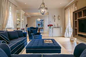 A living room with a sofa, ottoman, and a chair, a chandelier, and a television. - Villa Cesara - Casa del Sole (Vabriga)