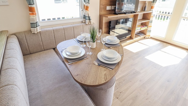 Un comedor con una mesa redonda dispuesta para cuatro personas, un sofá, un televisor y una estantería.