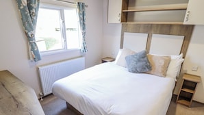 Un dormitorio con cama, un banco de madera, una ventana con cortinas, un radiador y un cabecero de madera.